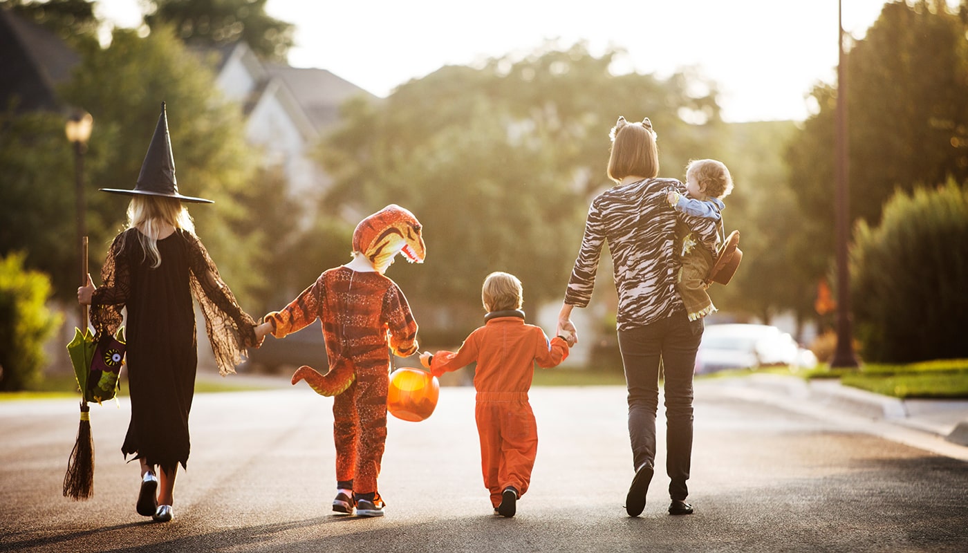 A family in costumes are walking down the street at dusk going trick-or-treating
