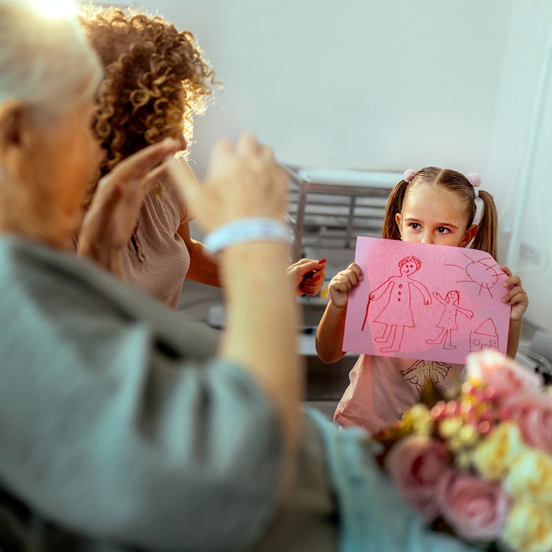 Free Get Well Soon Coloring Pages and 9 Ways Kids Can Help 4 A young girl holds up a cute drawing she made and shows it to her grandmother who is sick in the hospital.